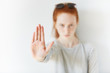 Isolated headshot of serious young redhead woman showing stop sign. Female wearing striped top looking at the camera with angry expression, gesturing with her palm. Selective focus. Film effect