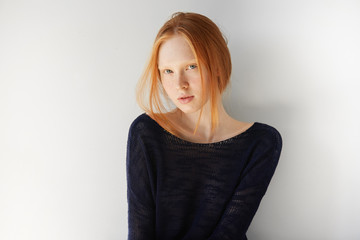 People and lifestyle concept. Cute young female with ginger hair, wearing stylish black top, looking at the camera with pretty smile against white copy space wall for your promotional content