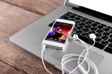 Canvas Print - White smart phone with headphones on laptop on wooden background