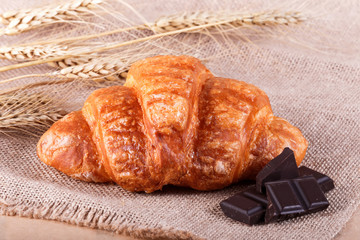 Wall Mural - Tasty croissant with chocolate on rustic background with spikelets. Pastries and bread in a bakery