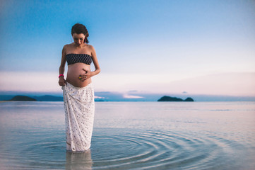 Young happy pregnant woman at the beach at sunset