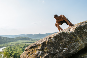 Emotional portrait of black african american man bodybuilder posing on the rock with blue sky background. Wild nature style