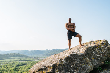 Handsome black african american athlete man on the rock in mountains. Beauty and perfection of human's body
