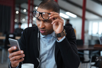 Busineessman touching his glasses and reading message on the smartphone
