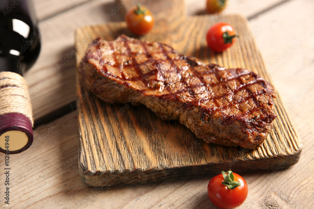 Grilled steak on cutting board with wine and cherry tomatoes, closeup