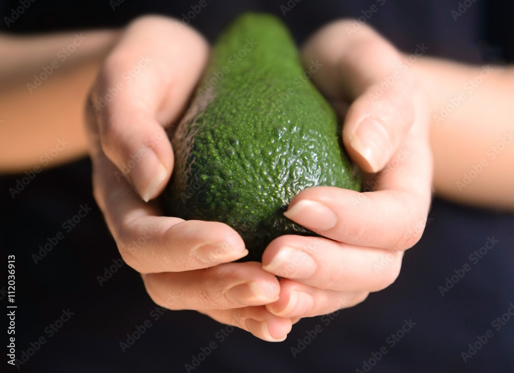 Female hands holding avocado on black background