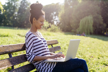 Young Woman Sitting On Park Bench Using Laptop
