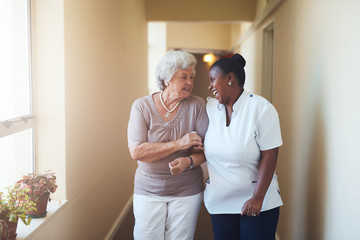 happy female caregiver and senior woman walking together