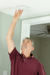 © Michael O'Keene - A handyman home owner is checking his house home smoke alarm by pushing the test button.