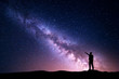 Milky Way with silhouette of a standing young man pointing finger in night starry sky on the mountain. Night landscape. Beautiful Universe, travel background with purple sky full of stars and light