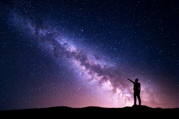 Wall Mural - milky way with silhouette of a standing young man pointing finger in night starry sky on the mountai