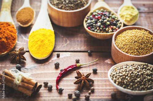 Fényképezés Beautiful colorful spices in wooden spoons and bowls on an old wooden brown table