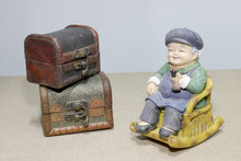 Lovely Grandparent Doll Siting Rocking Bamboo Chair With Old Old Treasure Chest On Wood Background. -still Life.