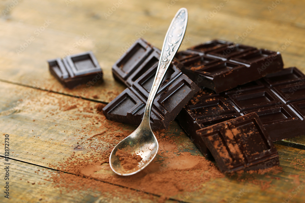 Slices of dark chocolate and spoon with cocoa powder on table