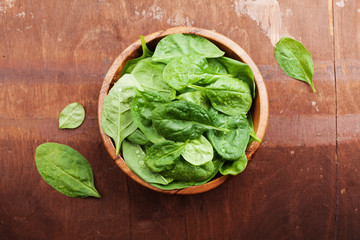 Wall Mural - Baby spinach leaves in wooden bowl on old rustic table, organic food, top view