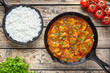 Traditional tikka masala chicken spicy meat Indian food with rice tomatoes and parsley in cast iron skillet on vintage wooden background