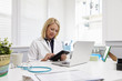 © Monkey Business - Female Doctor Sitting At Desk Using Digital Tablet In Office