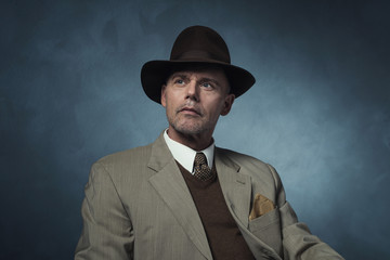 Fashionable retro 1940 business man with hat against gray wall.