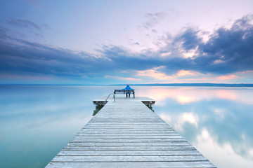 Canvas Print - Frau sitzt entspannt auf einer Bank am Steg am See