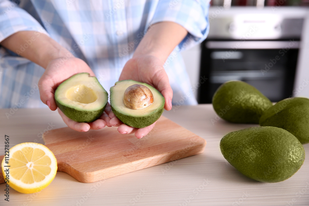 Woman holding fresh avocado in kitchen
