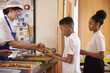 © Monkey Business - Dinner lady serving kids in a school cafeteria, side view