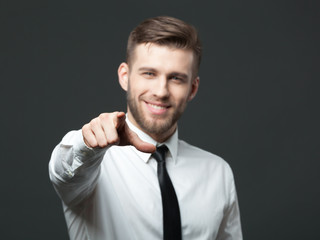 Young handsome businessman pointing at you  isolated on gray bac