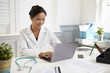 © Monkey Business - Female Doctor Sitting At Desk Working At Laptop In Office