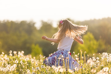 Girl running on the field of dandelions on summer sunset. Beautiful little kid girl  dancing on dandelion meadow with summer sunset. Summer fun outdoors.