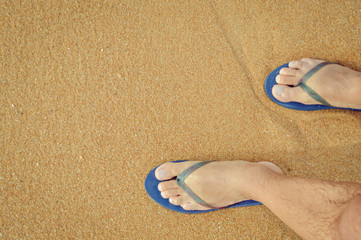 Wall Mural - Top view close up of man wearing blue flip flops walking along tropical exotic ocean beach