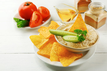 Wall Mural - Ceramic bowl of tasty hummus with chips, oil and vegetables on table