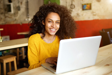 Wall Mural - Smiling young african woman sitting in a cafe with laptop