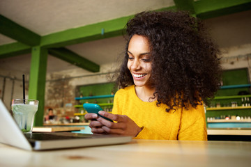 Wall Mural - Cheerful young woman using mobile phone in a cafe