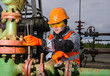 © polina_petrenko - Woman engineer in the oil field repairing wellhead with the wrench wearing orange helmet and work clothes. Oil and gas concept.