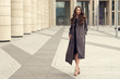 © Dmitry Tsvetkov - Young elegant girl posing at city street. Pretty beautiful business woman in elegant black dress and gray coat against city background. Full length horizontal portrait.