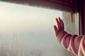 Child hand on fogged glass looking through the window, closeup