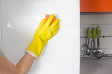 Wall Mural - A Woman hand in yellow rubber protective glove cleaning white door of refrigerator in the kitchen