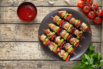 Traditional turkey or chicken meat skewers shish kebab with onion and tomatoes, parsley, ketchup in clay dish on rustic wooden table background. Barbecue grill food.