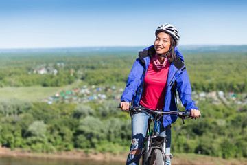 Cheerful beautiful young woman with a bike on a field with helmet smiling