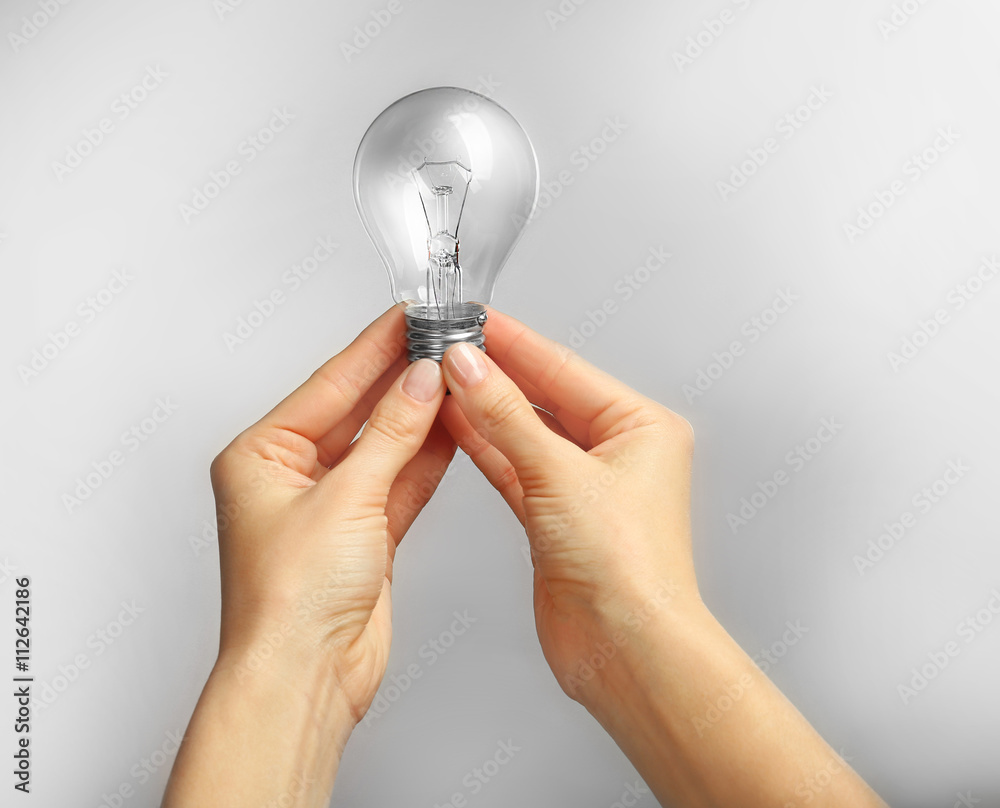 Woman hands holding bulb on grey background