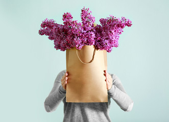 Poster - Woman holding bouquet of purple lilac flowers in paper bag on grey background