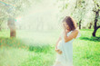 Pregnant woman in the apple orchard is holding tummy
