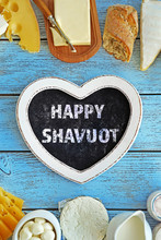 Text Happy Shavuot In Frame Of Fresh Dairy Products On Blue Wooden Table
