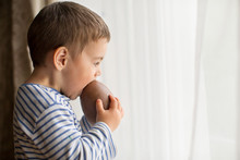 Boy Standing By Window Eating A Large Chocolate Easter Egg
