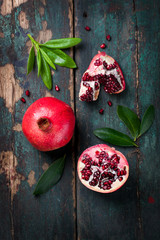 Wall Mural - Fresh juicy pomegranate - whole and cut, with leaves on a wooden vintage background, top view, horizontal, with copy space