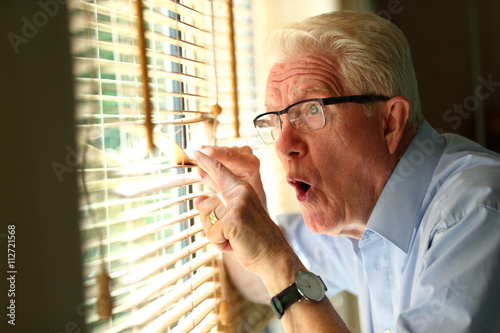 Fotografía curiosity/ curious senior man looking through the blinds of his window