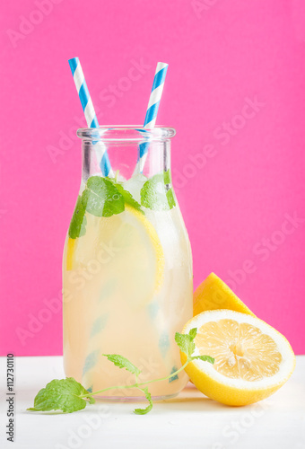 Fotografía Bottle of homemade lemonade with mint, ice, lemons, paper straws and bright purp