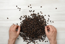 Close-up Hands Of Man On A Wooden Surface With Spreaded Coffee Beans