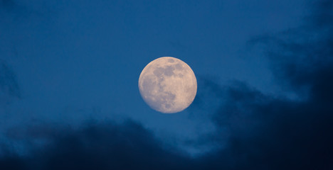 full glowing moon closeup on blue sky and dark misty clouds