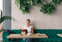 Enjoyoing Coffee Break. Woman Reading Book In Cafeteria