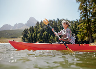 Wall Mural - Mature woman paddling a kayak in lake